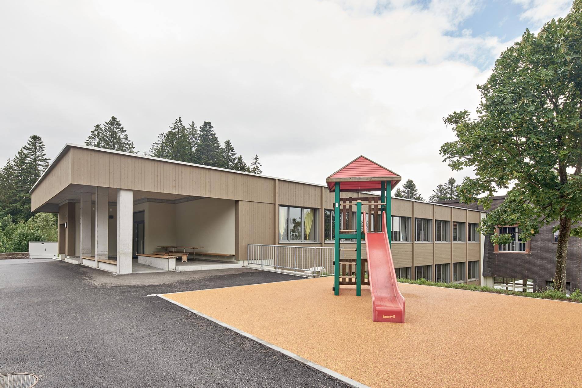 Spielplatz mit Rutsche und Klettergerüst neben einem Gebäude.