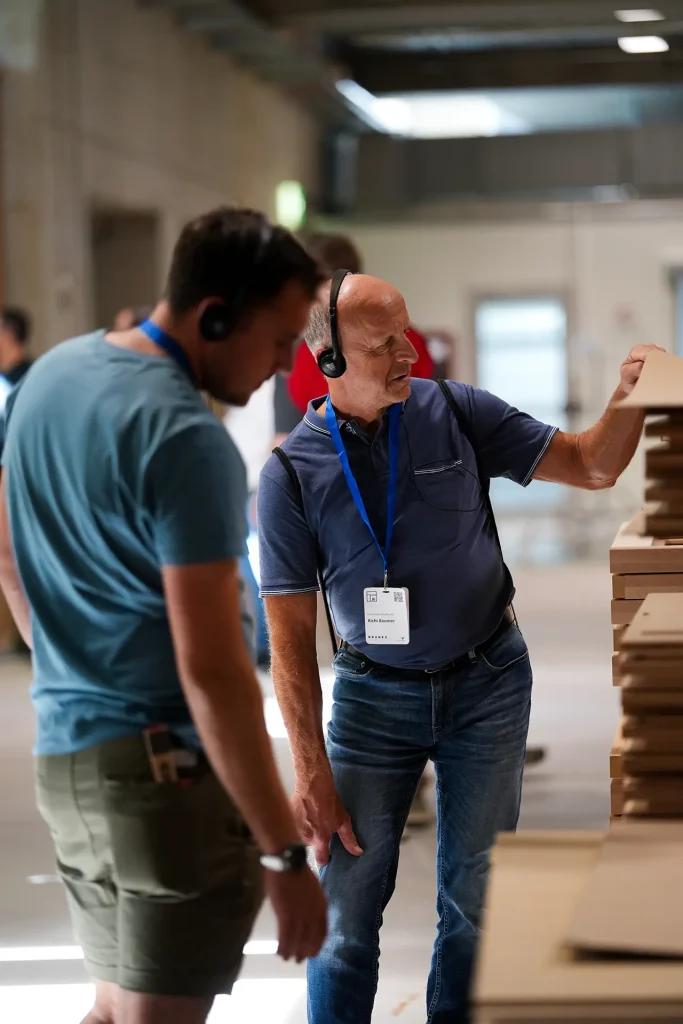 Zwei Männer beobachten Materialstapel in einem Workshop.